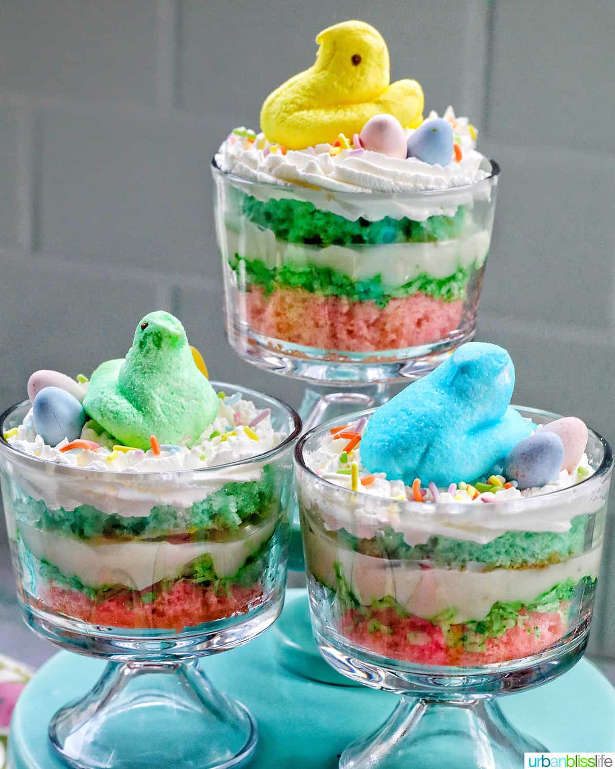 Set of Easter trifles with layers of pastel colored cake, shredded coconut, vanilla pudding, and whipped cream, topped with colorful Easter candies.