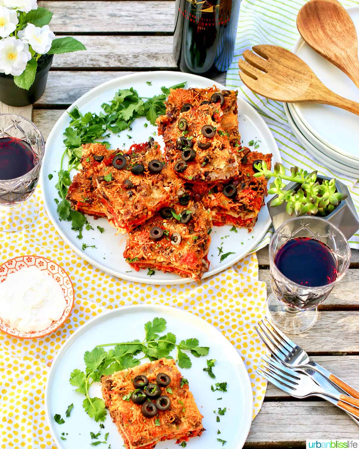 two plates with slices of Mexican lasagna stacked next to glasses of red wine.