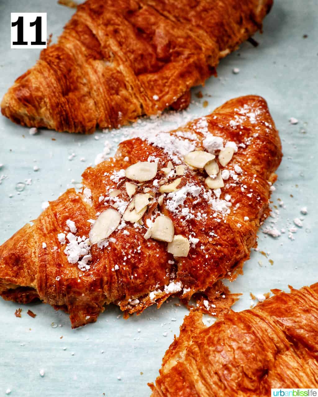three almond croissants on a baking sheet.