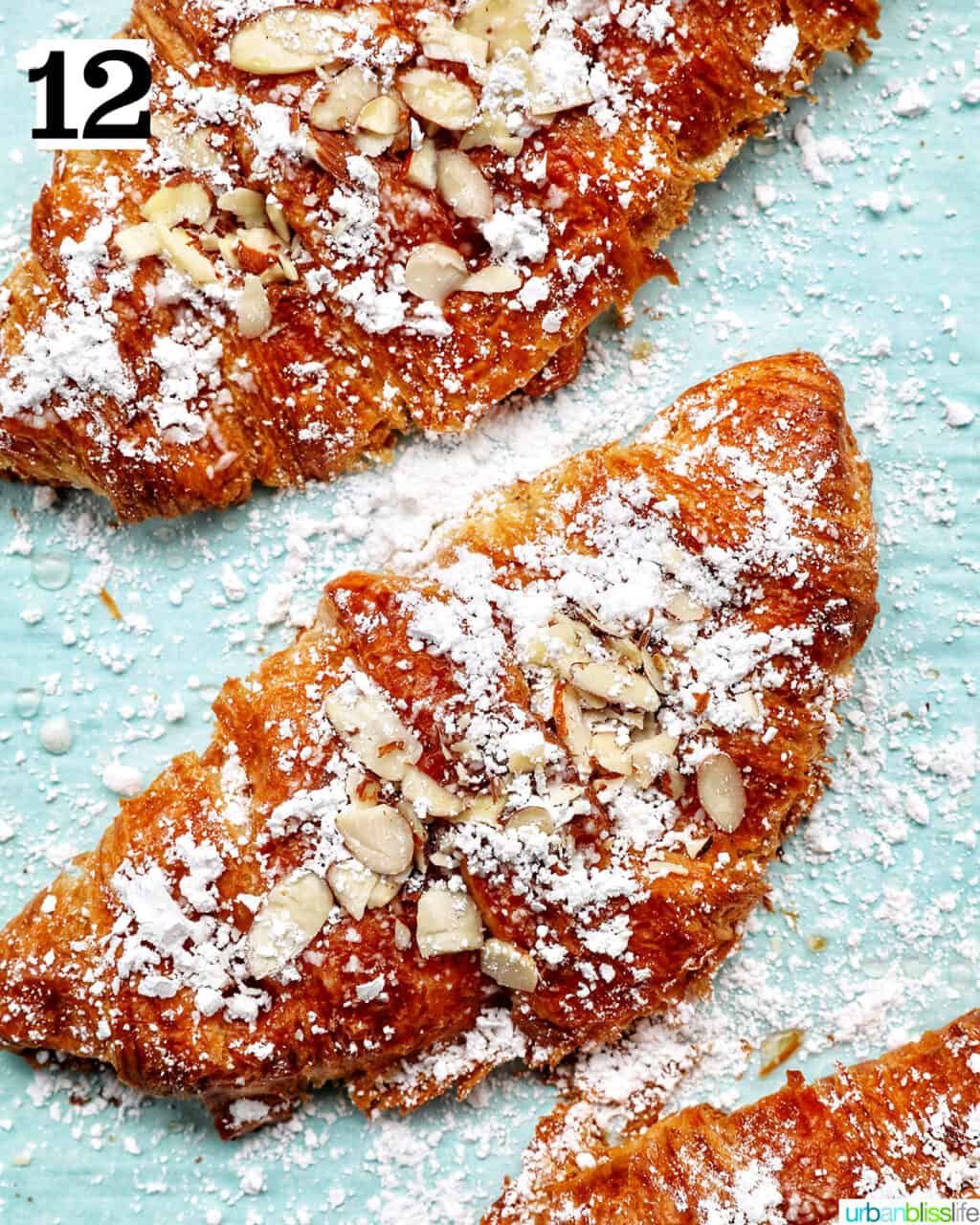 three almond croissants on a baking sheet.