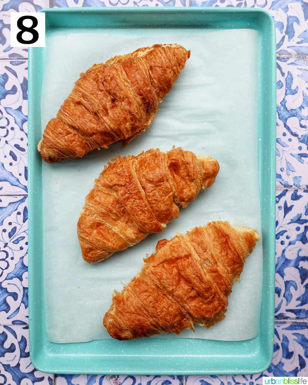 three almond croissants on a prepared baking sheet.