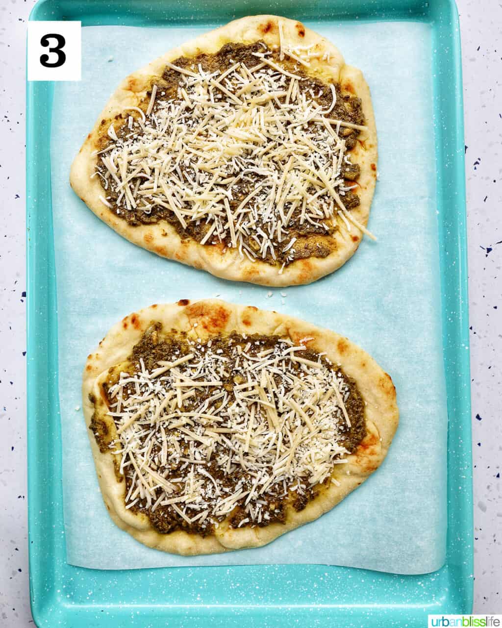 two naan flatbreads with pesto and mozzarella cheese on a baking sheet.