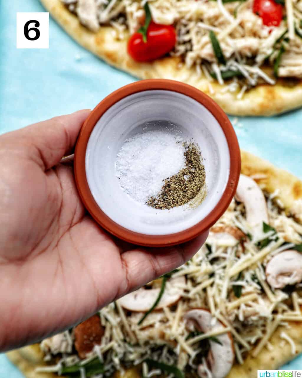 hand holding a bowl of salt and pepper over chicken pesto flatbread.