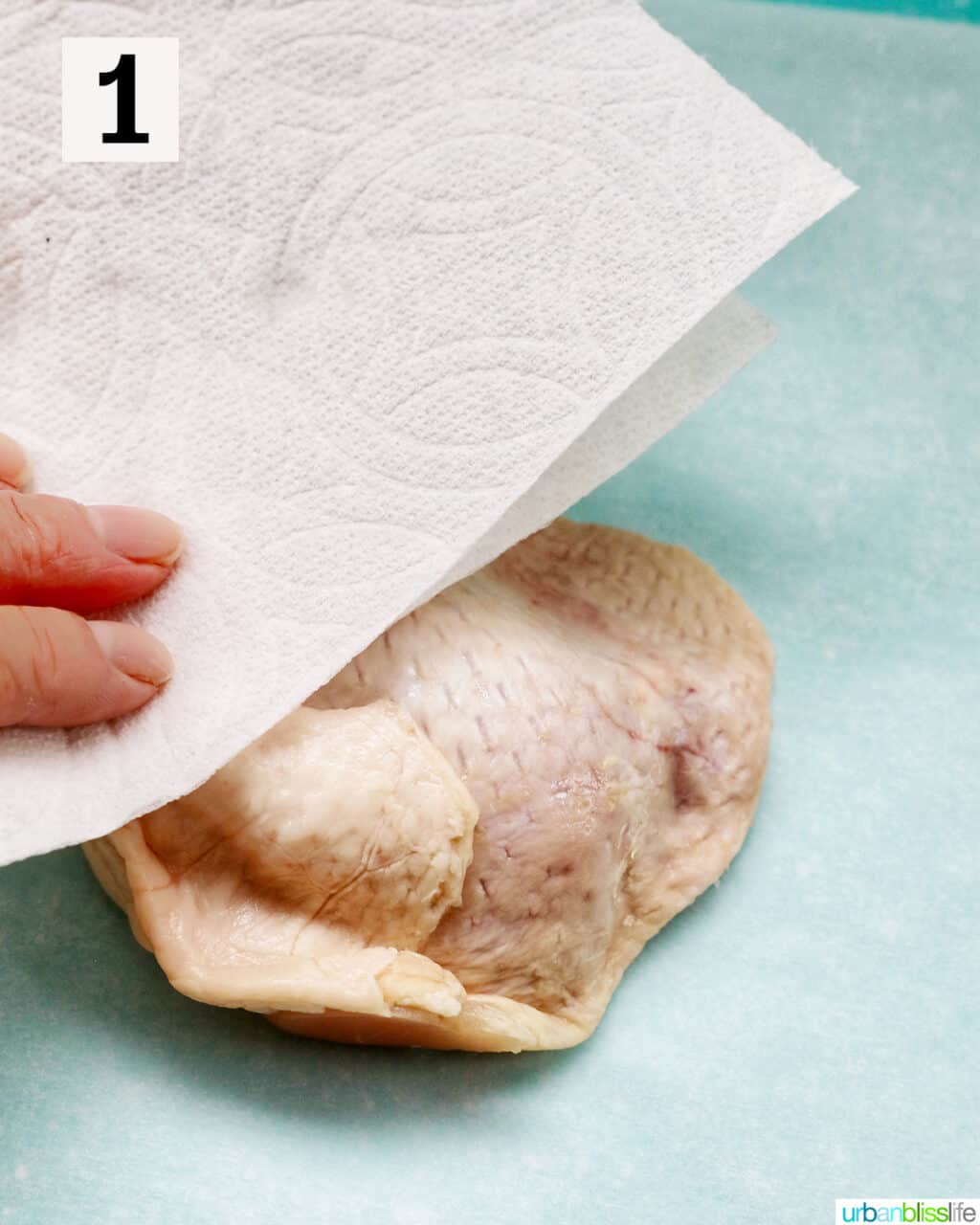hand patting raw chicken with a paper towel.