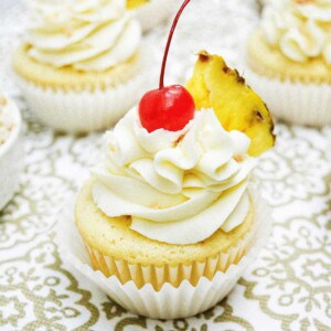pina colada cupcakes with slice of pineapple on patterned table.