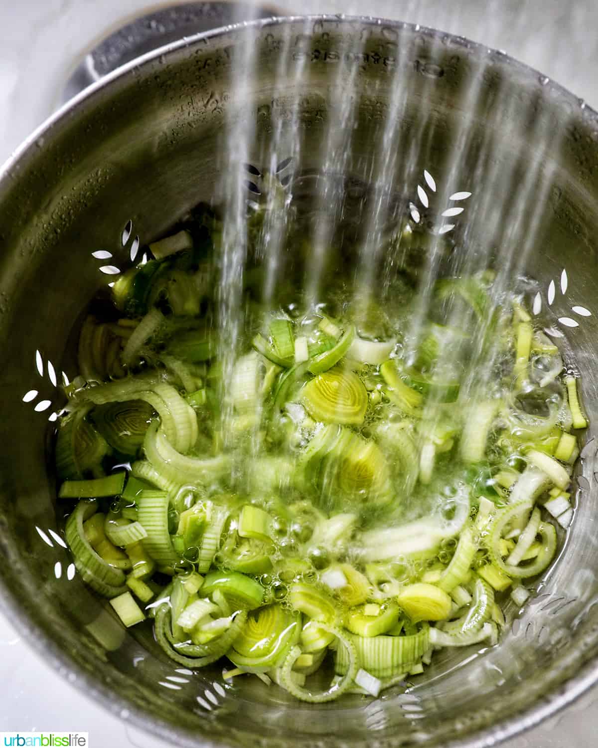 water rinsing sliced leeks in a collander in a sink.