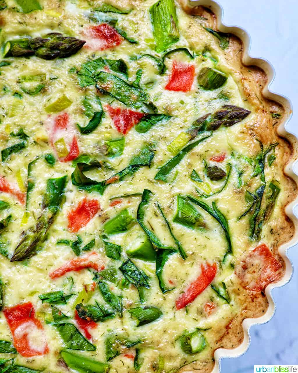 Half of a quiche in a pie pan with salmon, asparagus, and leeks.