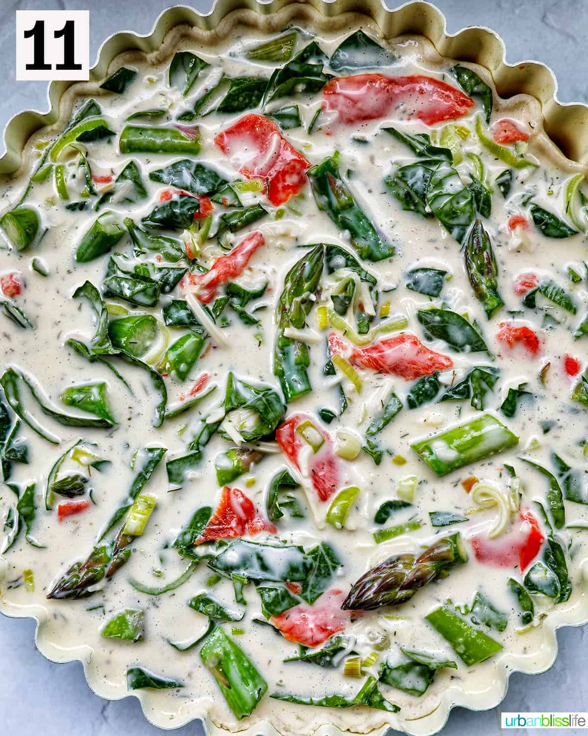 quiche filling with smoked salmon, asparagus, and leeks in a pie plate ready to bake.