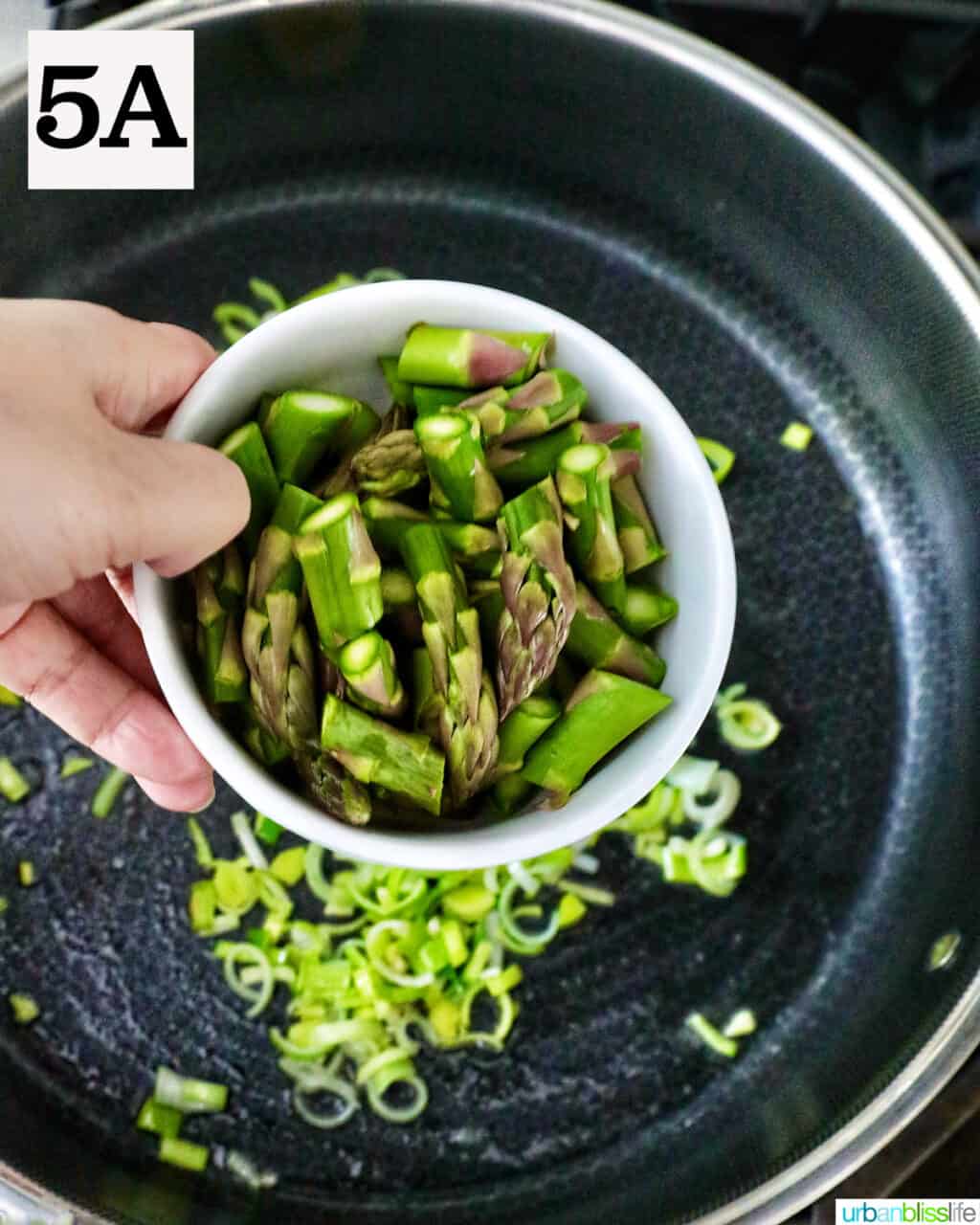 hand holding a bowl of sliced asparagus over a pan.