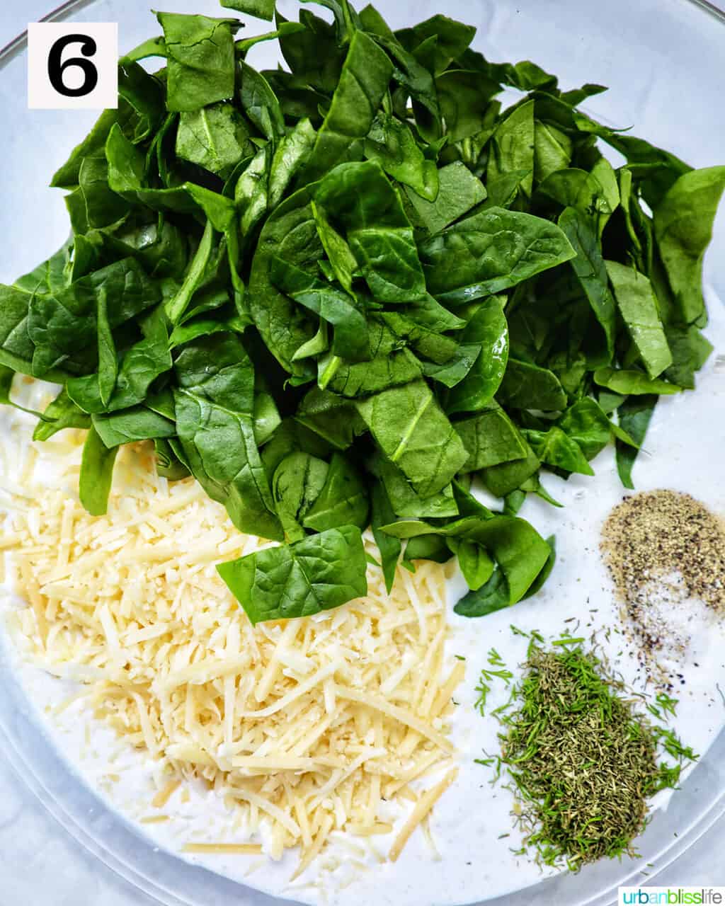 bowl with sliced spinach, shredded cheese, and herbs and seasonings.