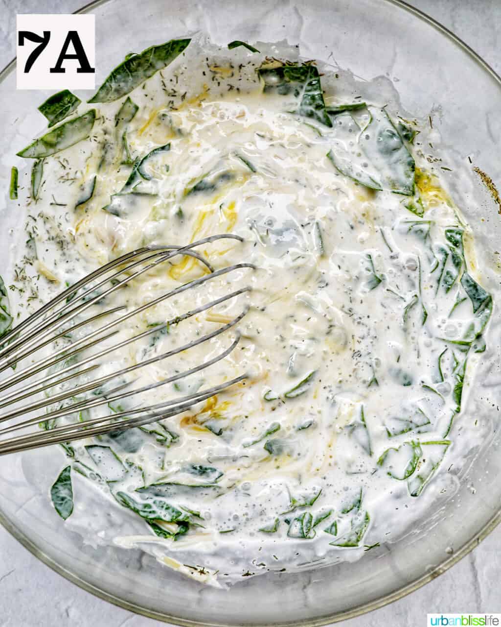 whisk in a bowl of quiche filling with green herbs and vegetables.