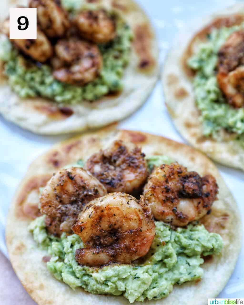 three tortillas topped with guacamole and seasoned shrimp.