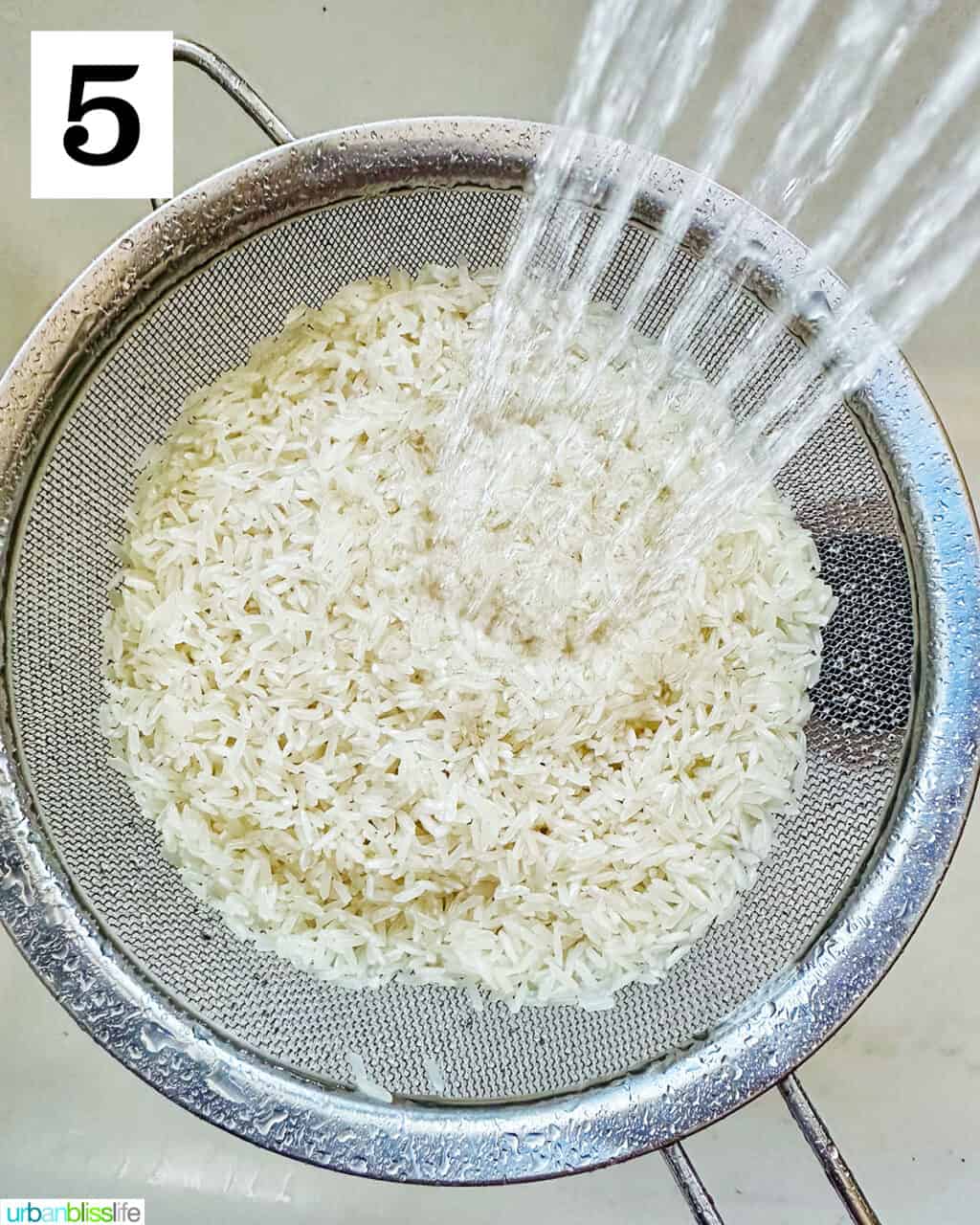 water rinsing rice in a strainer over a sink.