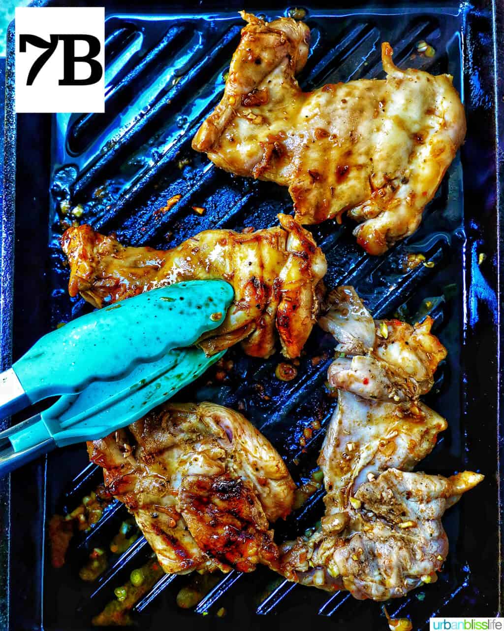 chicken thighs cooking on a grill pan with blue tongs on the side.