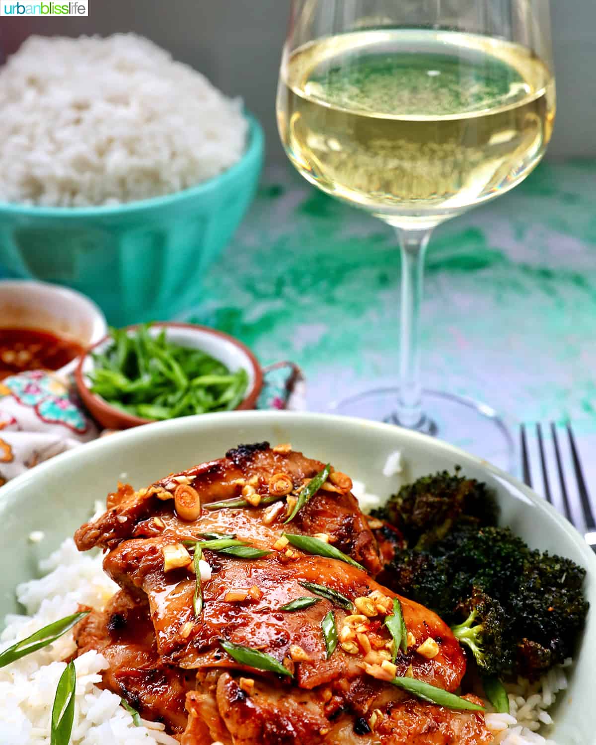 Plate with a stack of Thai Lemongrass Chicken over rice and sliced green onion garnish and a glass of white wine.
