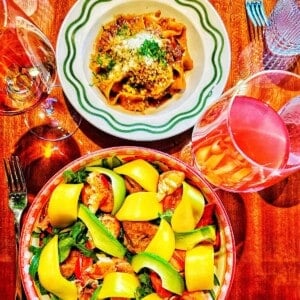 large bowl of lobster mango salad, bowl of pappardelle ragu pasta, and two glasses of wine at Bad Roman restaurant in New York City.