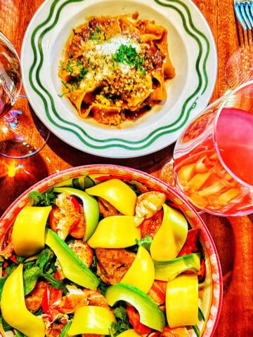 large bowl of lobster mango salad, bowl of pappardelle ragu pasta, and two glasses of wine at Bad Roman restaurant in New York City.