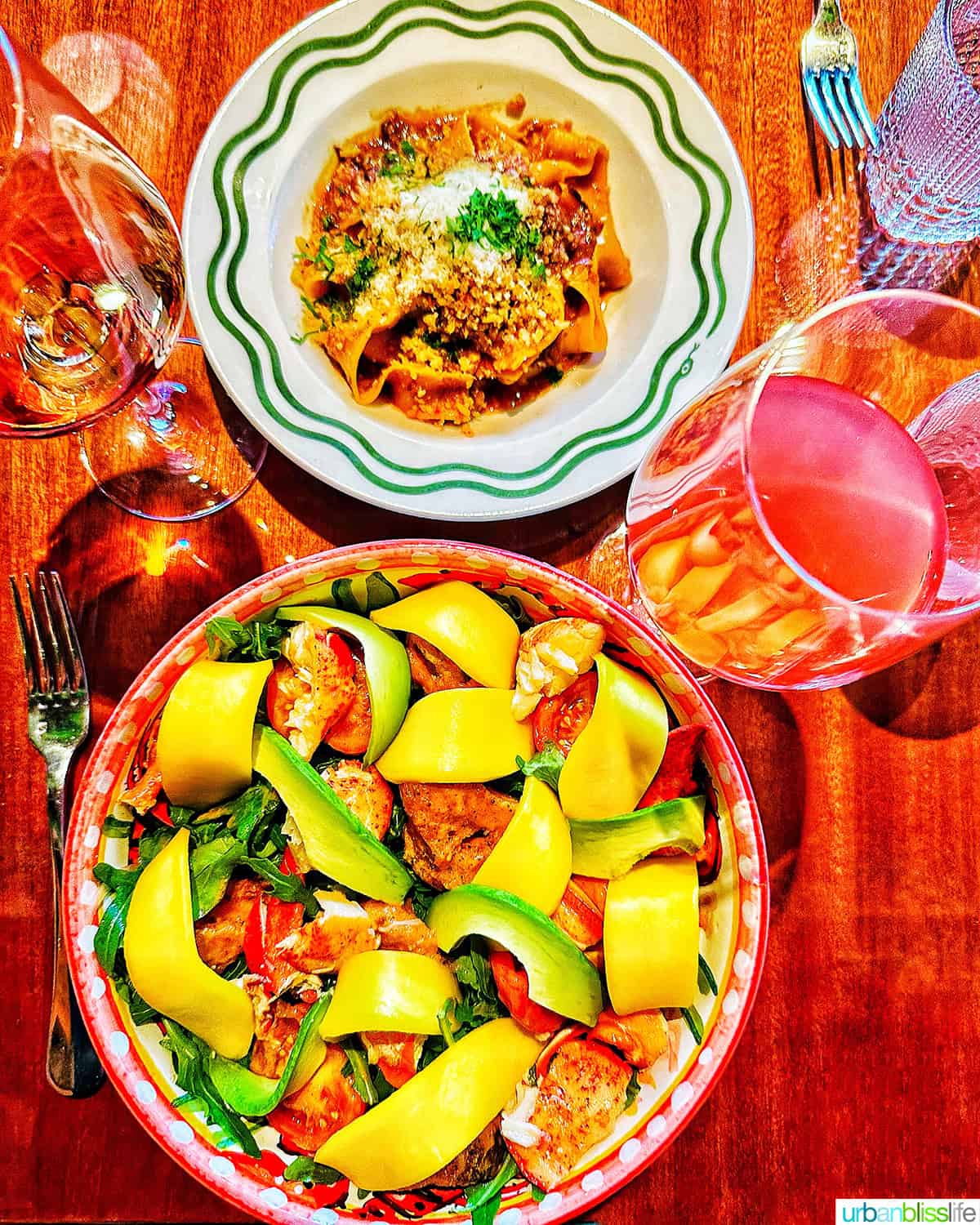 large bowl of lobster mango salad, bowl of pappardelle ragu pasta, and two glasses of wine at Bad Roman restaurant in New York City.