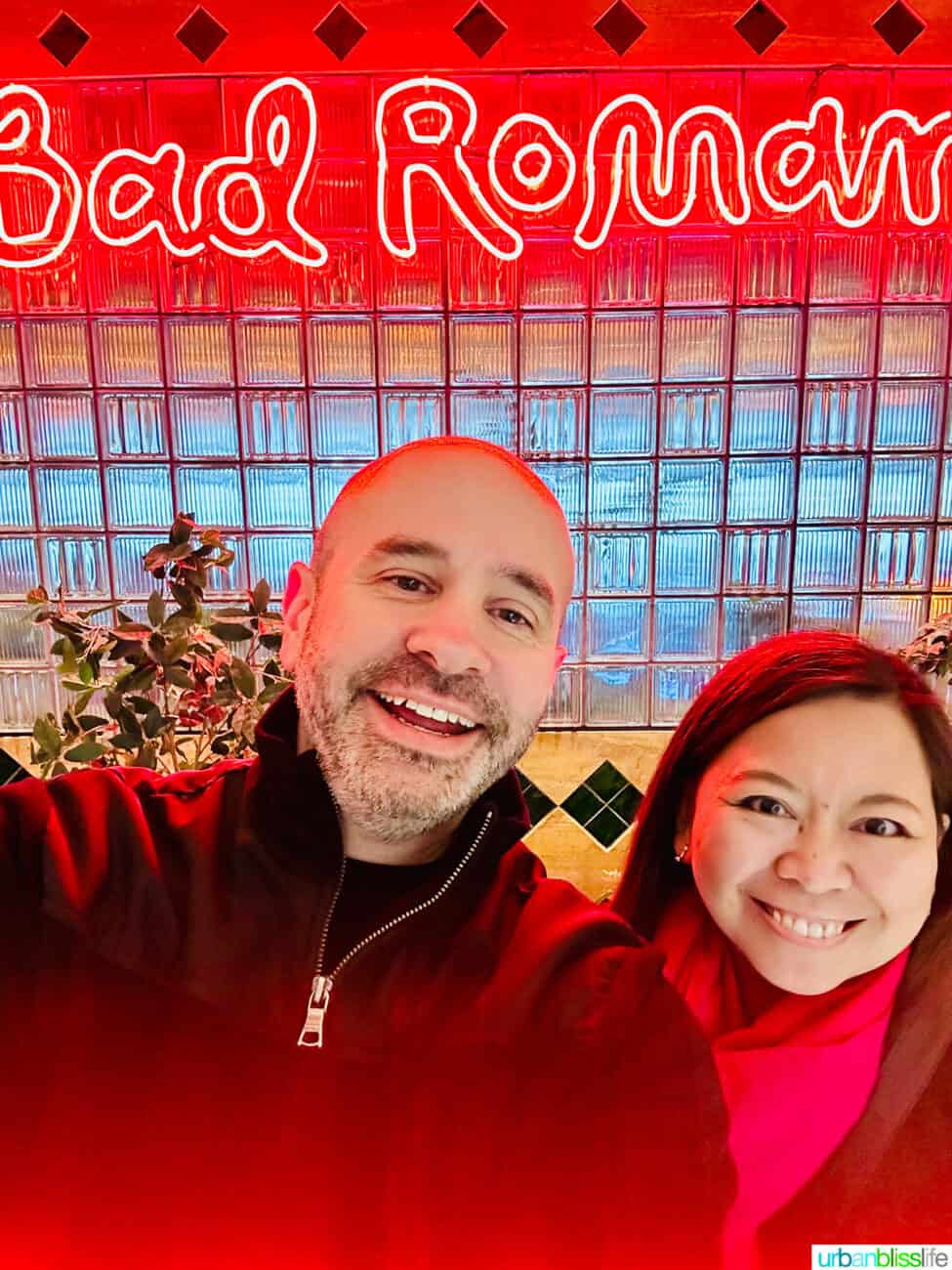 Alain Schotland and Marlynn Jayme Schotland in front of a neon sign at Bad Roman restaurant in New York City.