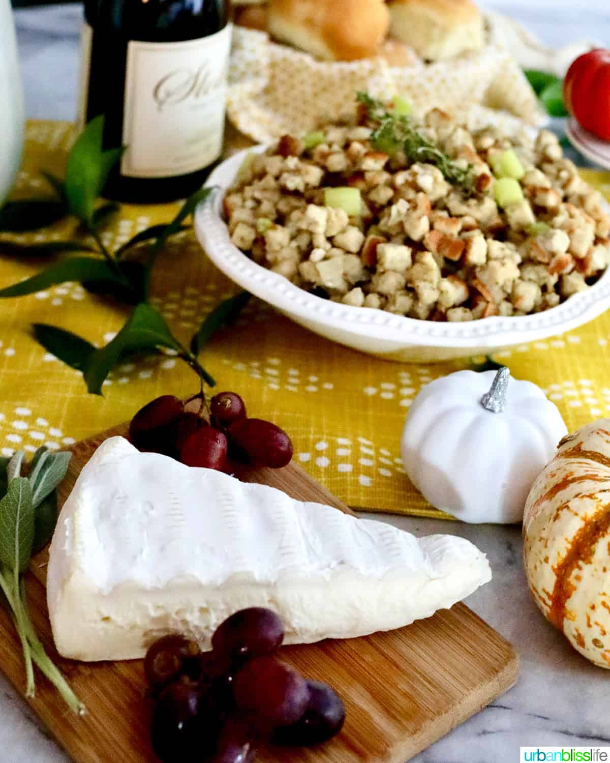brie cheese wedge on a board with grapes and Thanksgiving stuffing in the background.