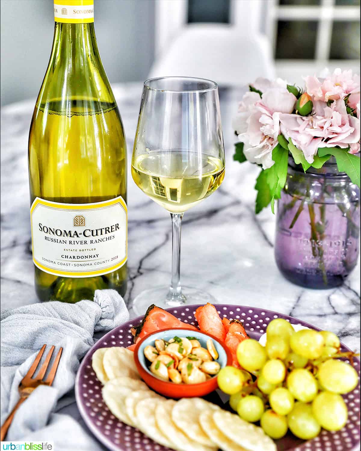bottle and glass of Chardonnay white wine with plate of snacks.
