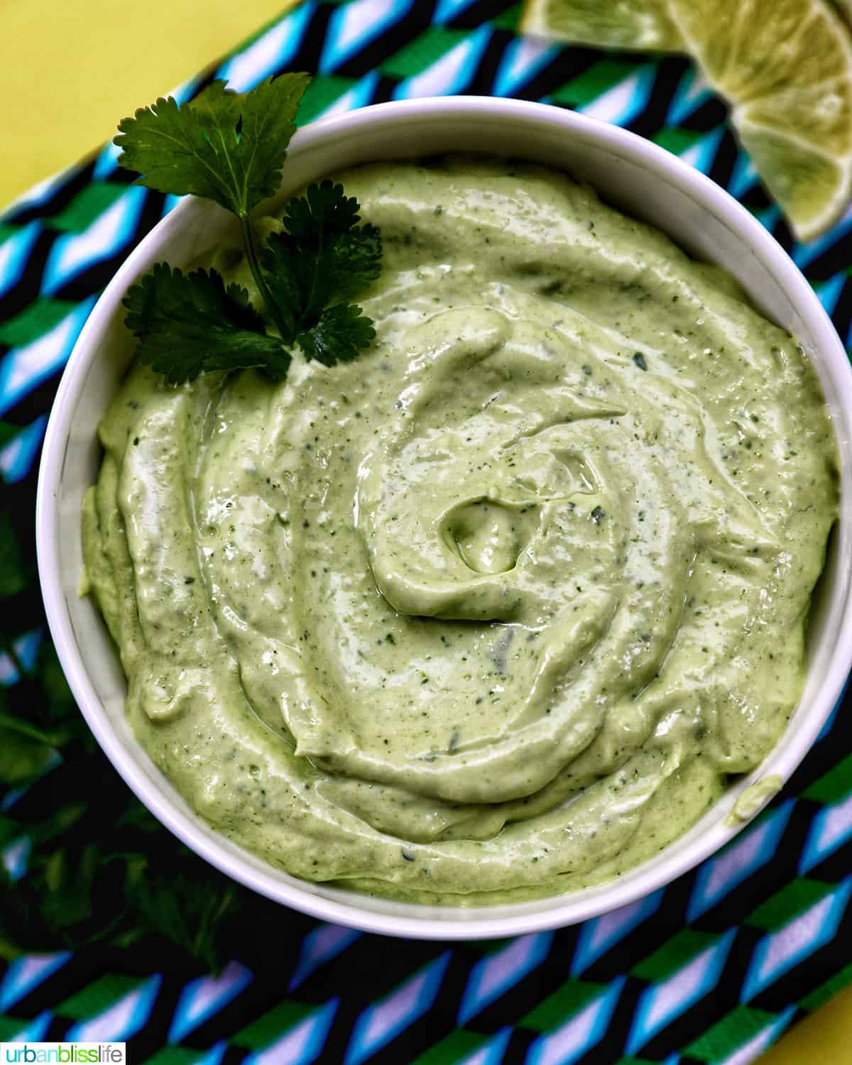 bowl of avocado cilantro lime crema on a colorful modern napkin with garnish of cilantro leaves.