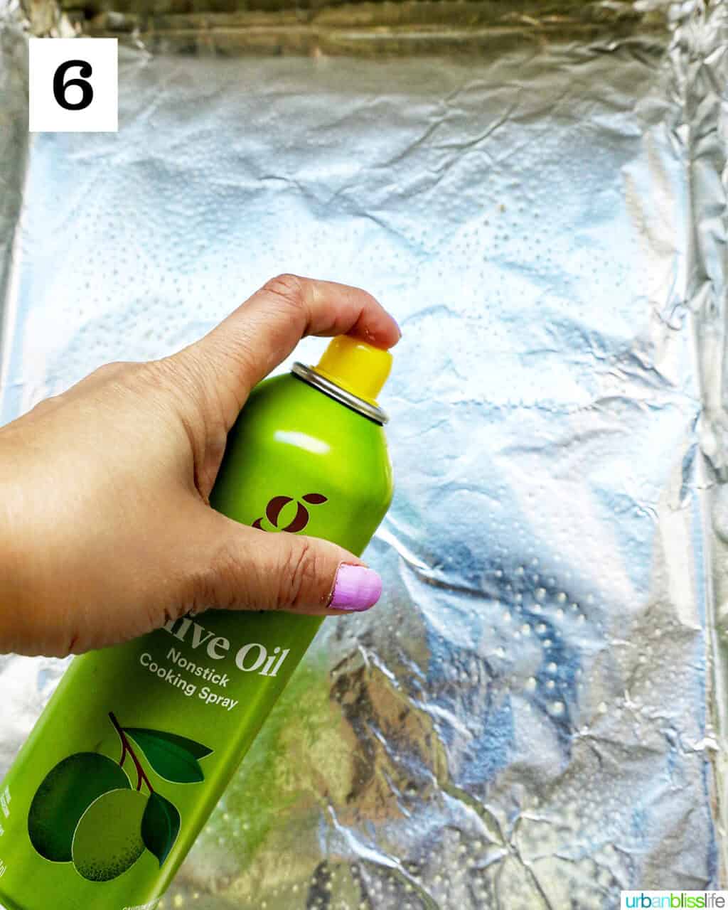 hand spraying cooking spray over aluminum foil.