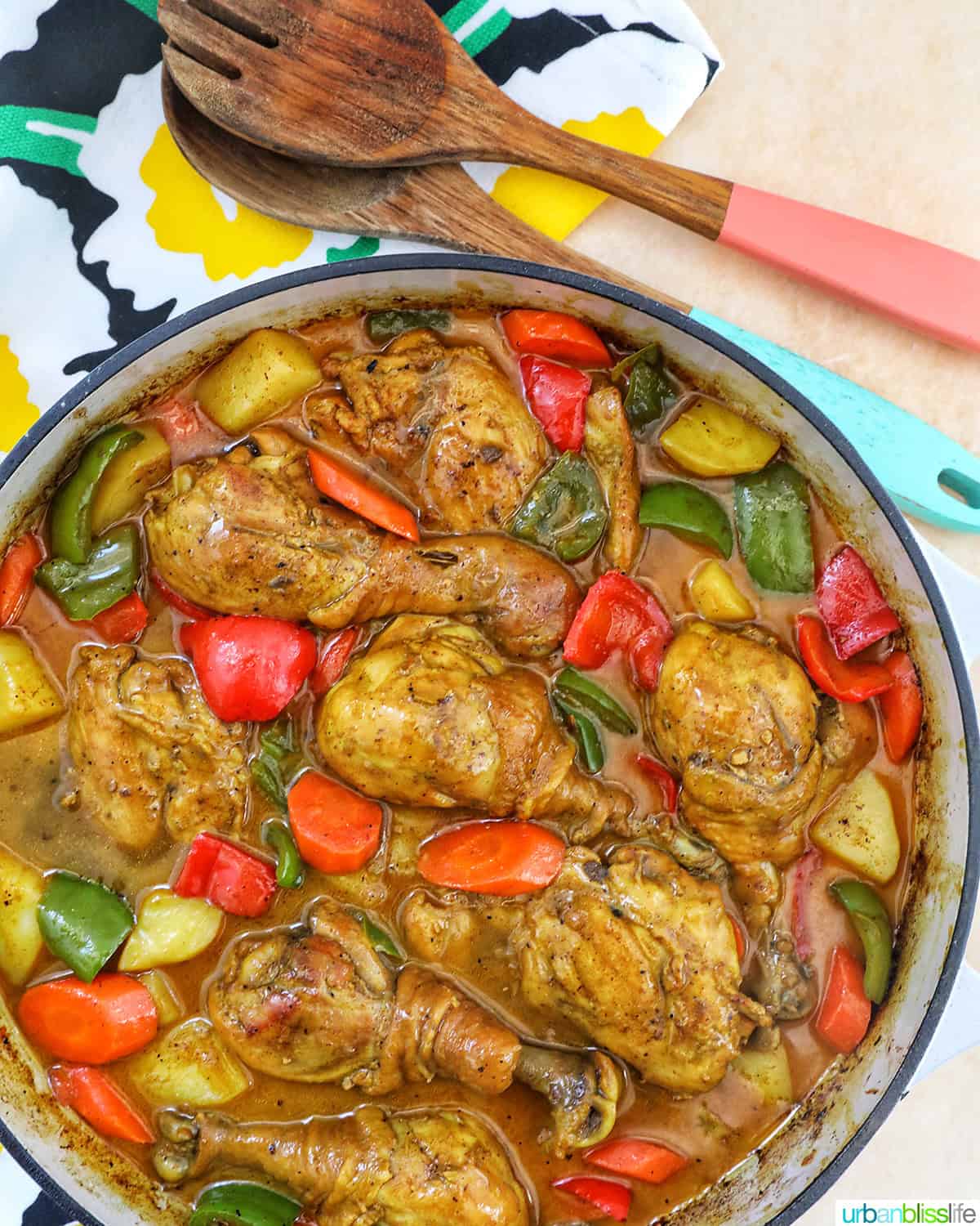 Filipino Chicken Curry with vegetables in a large pan with wooden utensils.
