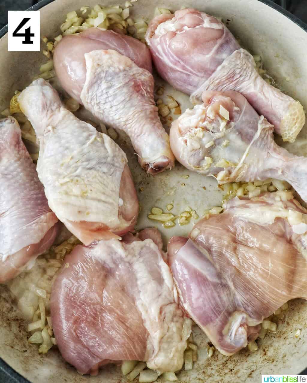 chicken pieces added to a large pan with garlic and onions.