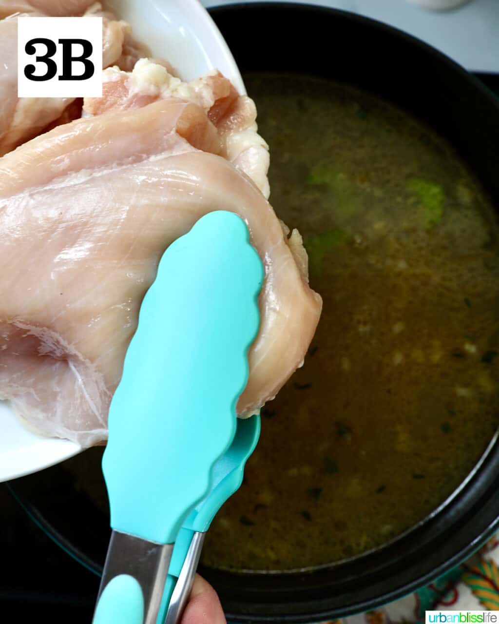 tongs holding raw chicken going into a large pot.