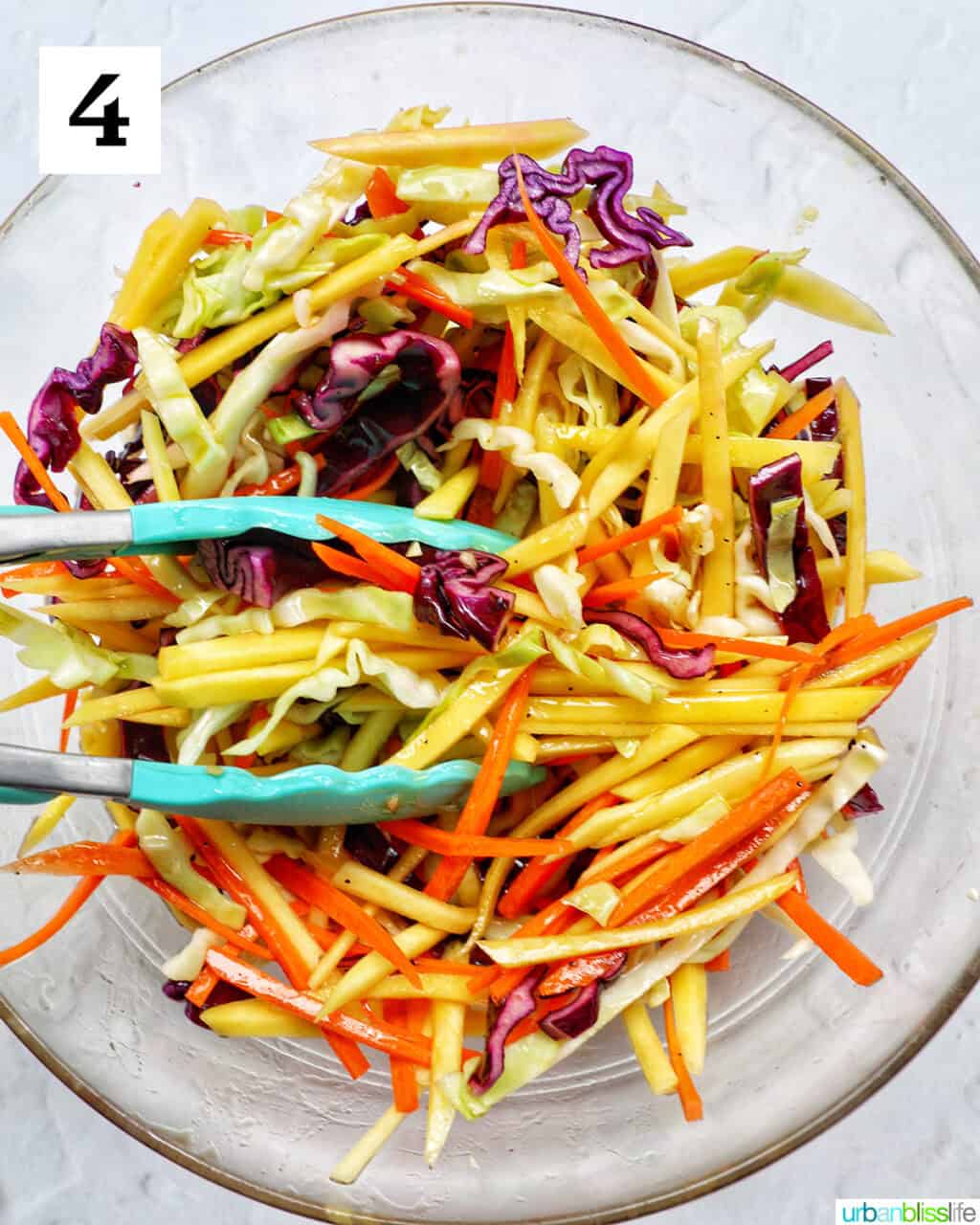mango slaw with fresh herbs and kitchen tongs in a bowl.