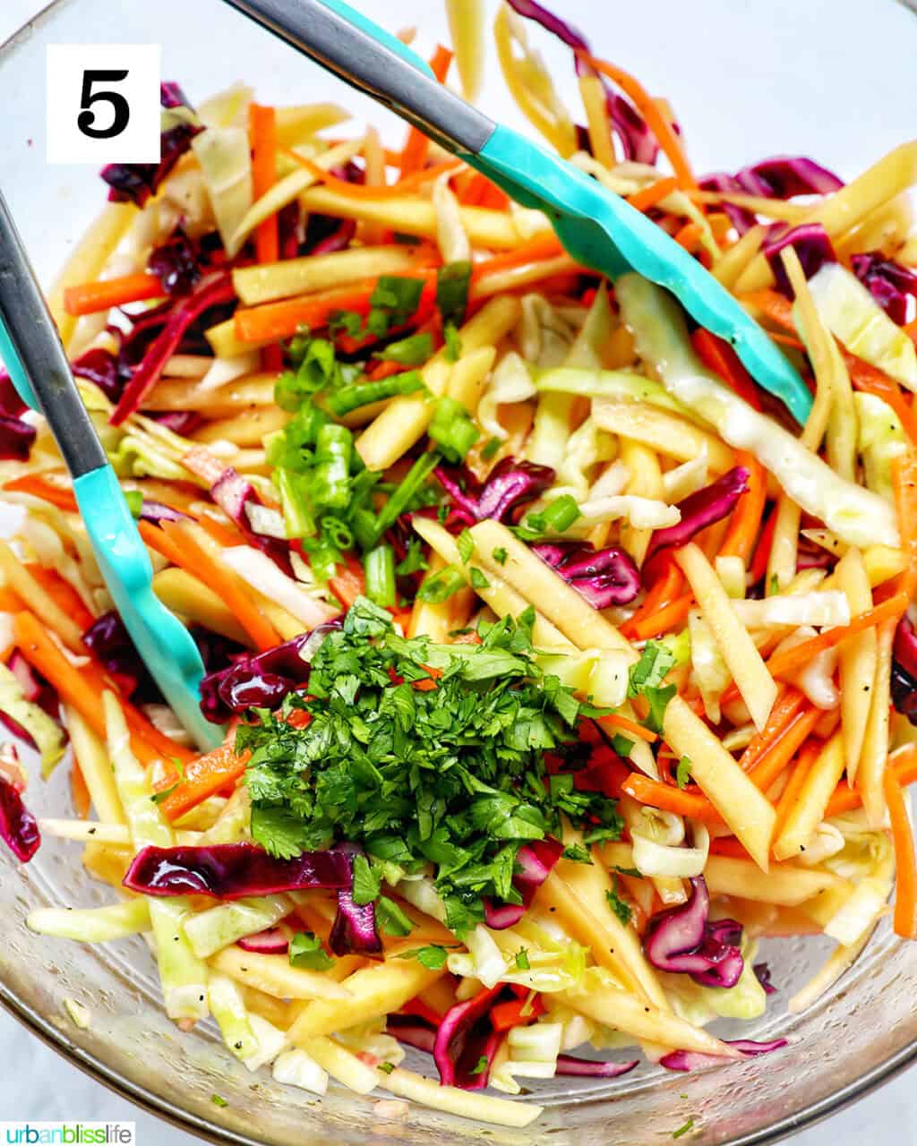 mango slaw with fresh herbs and kitchen tongs in a bowl.