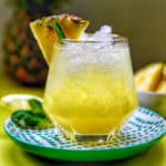 glass of pineapple mocktail with mint leaves and pineapple slice garnish.