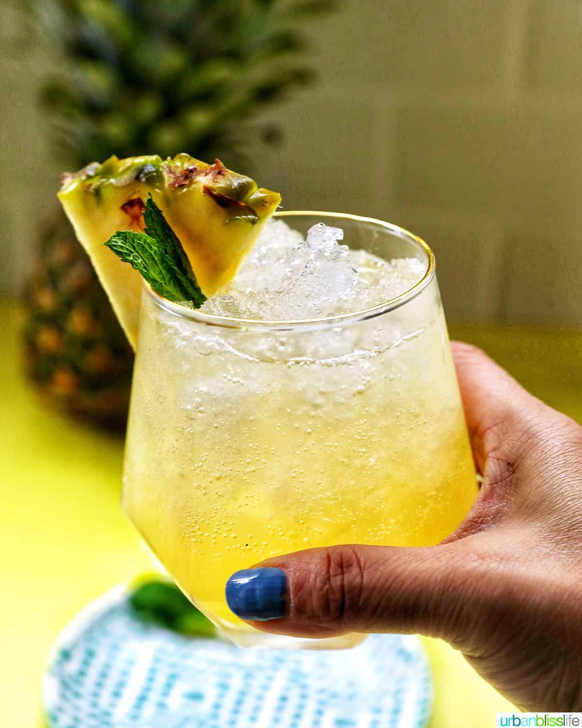 hand holding a glass of pineapple mocktail with mint leaves and pineapple slice garnish.