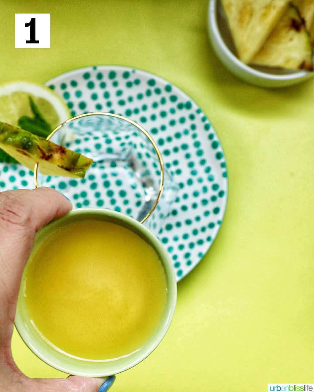 hand holding a bowl of pineapple juice over a glass.