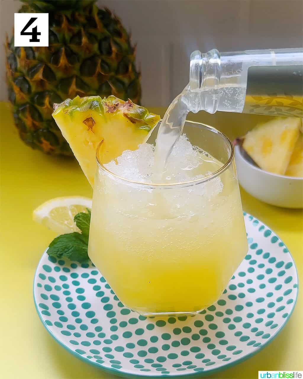 pouring ginger beer into a glass of pineapple mocktail with mint leaves and pineapple slice garnish.