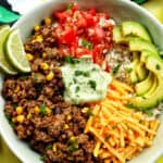 taco bowl with ground beef, beans, cheese, pico de gallo, avocado, rice, avocado cilantro lime crema.