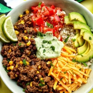 taco bowl with ground beef, beans, cheese, pico de gallo, avocado, rice, avocado cilantro lime crema.