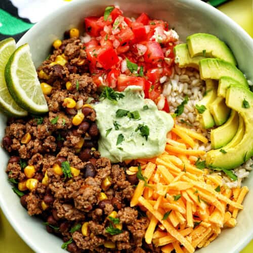 taco bowl with ground beef, beans, cheese, pico de gallo, avocado, rice, avocado cilantro lime crema.