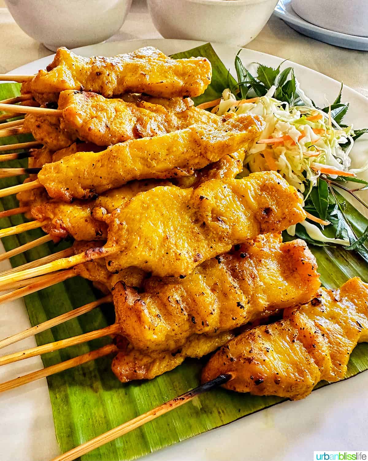 stacks of chicken satay skewers on banana leaves.