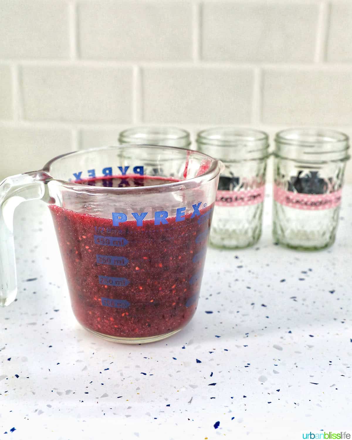 blackberry freezer jam in a large measuring cup next to empty mason jars.