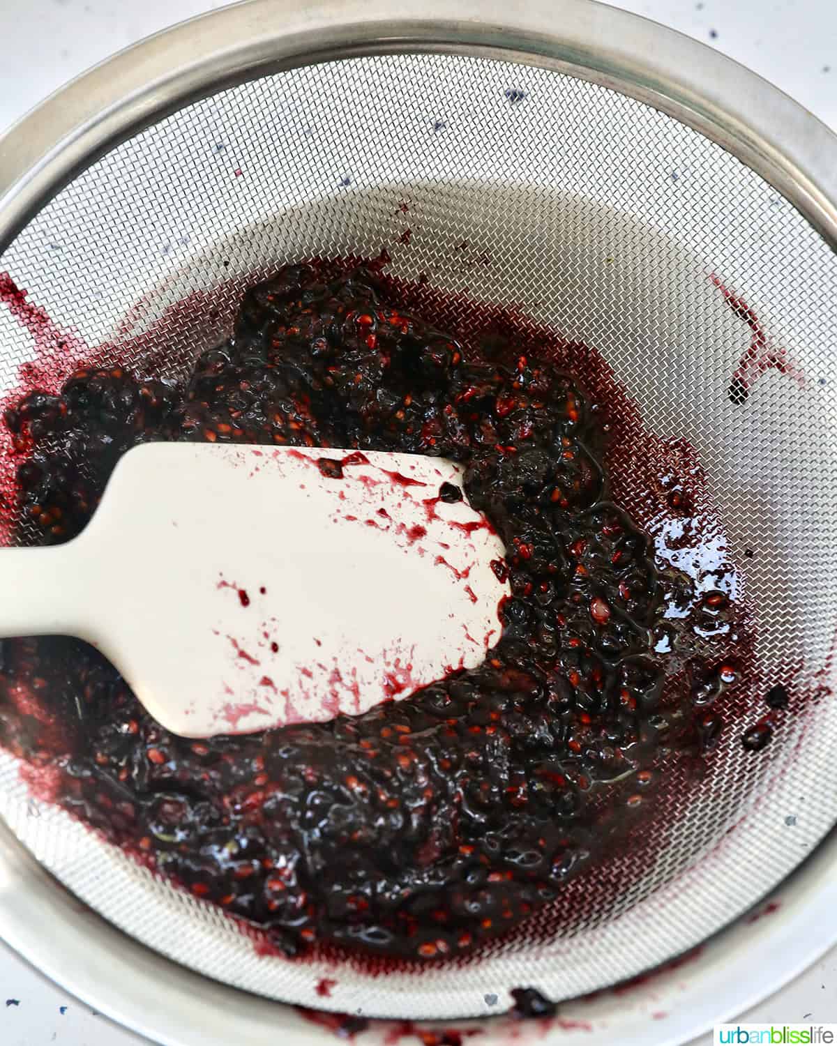 spatula straining blackberry freezer jam through a sieve.