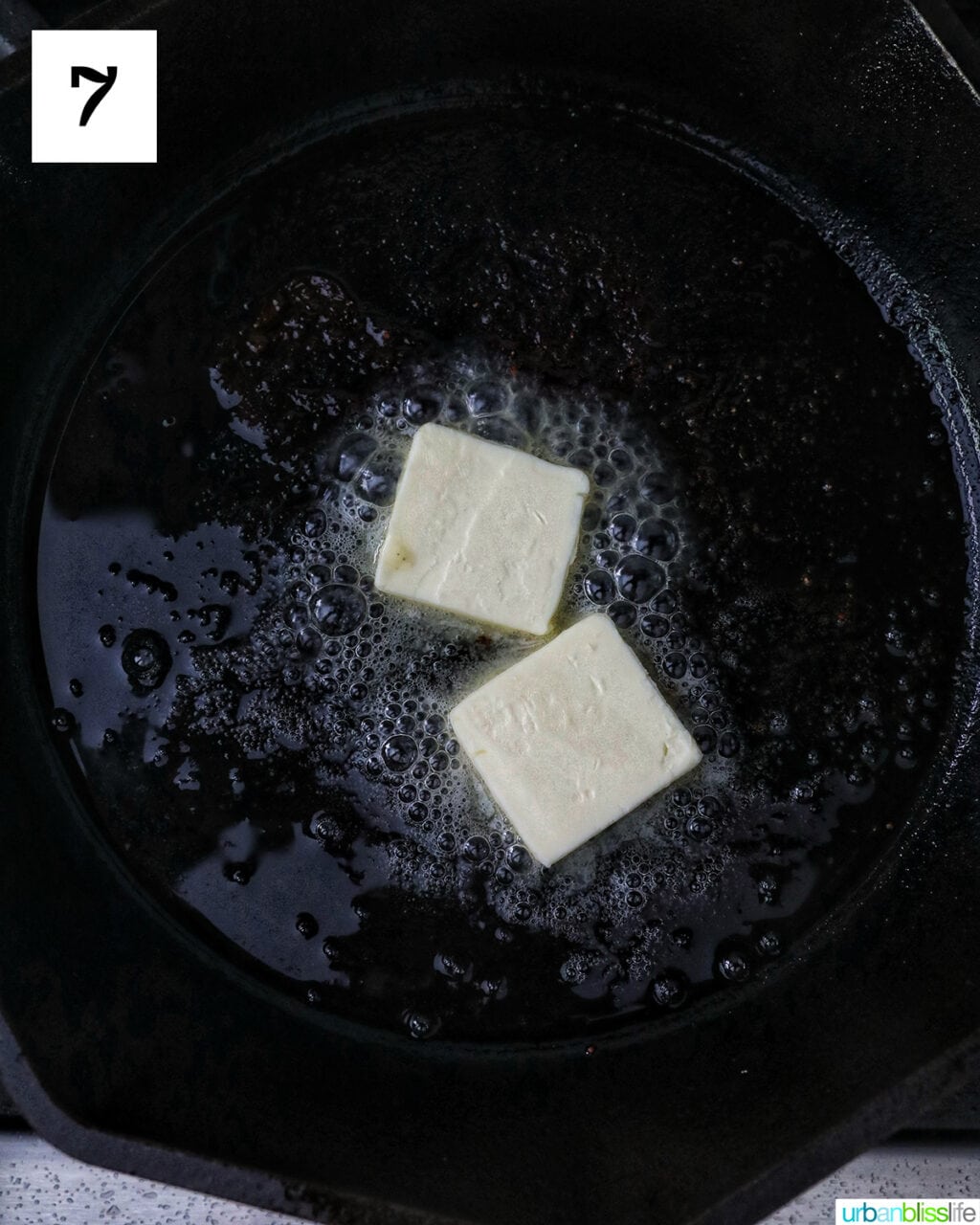 two pats of butter melting in a cast iron skillet.
