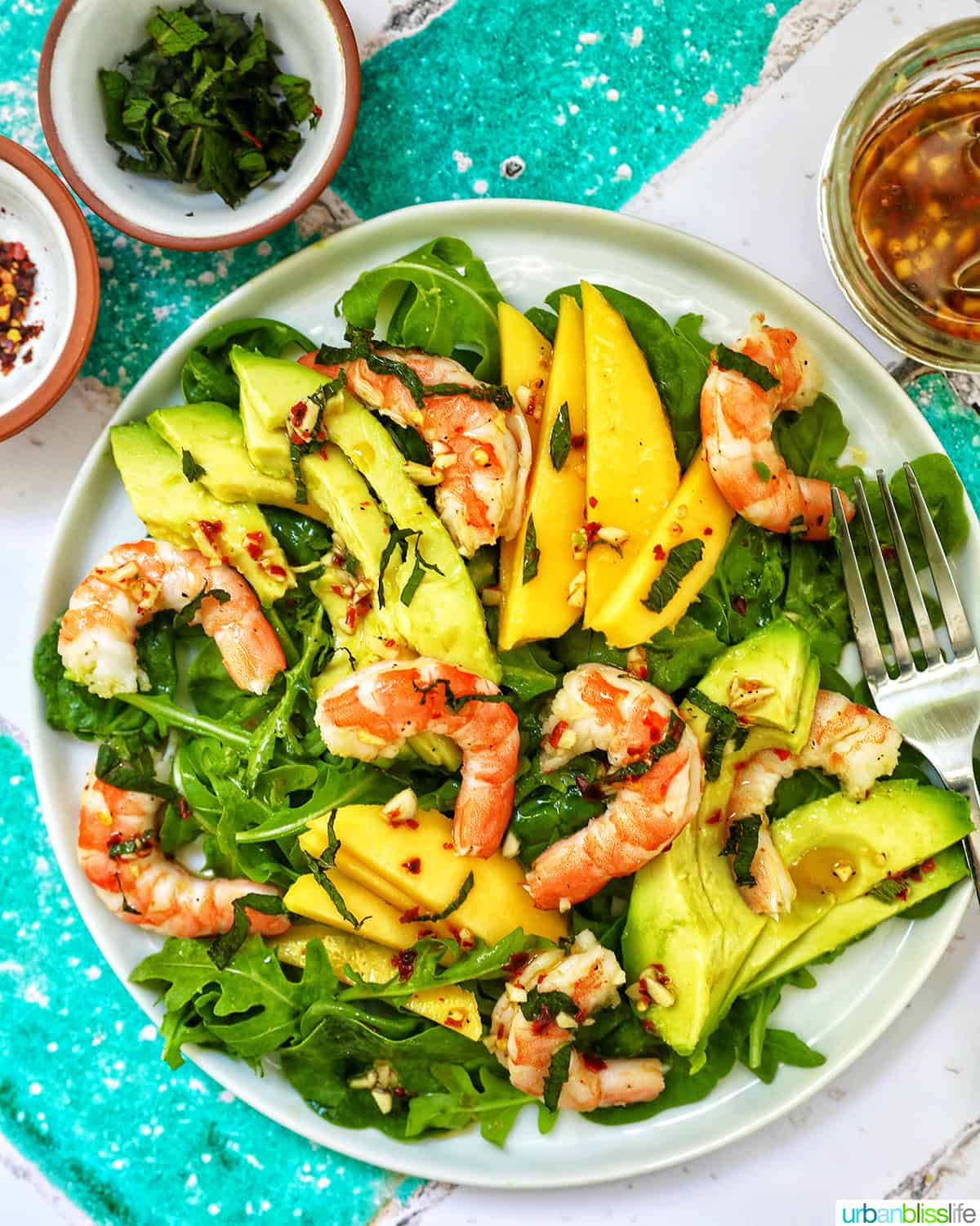 mango avocado prawn salad with sides of garnishes and a fork.