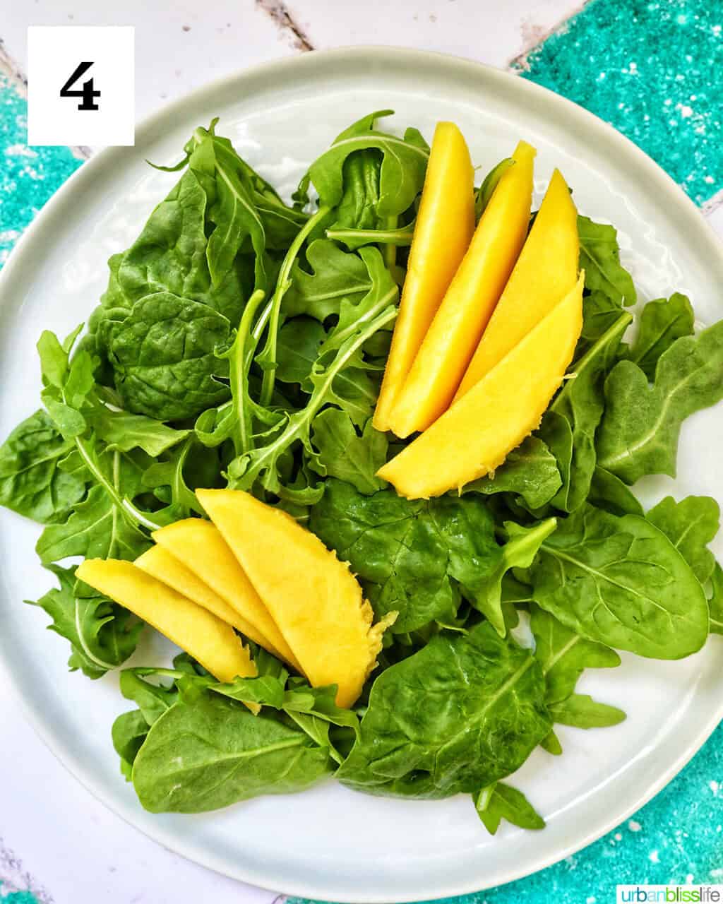 white plate with mixed greens and mango.