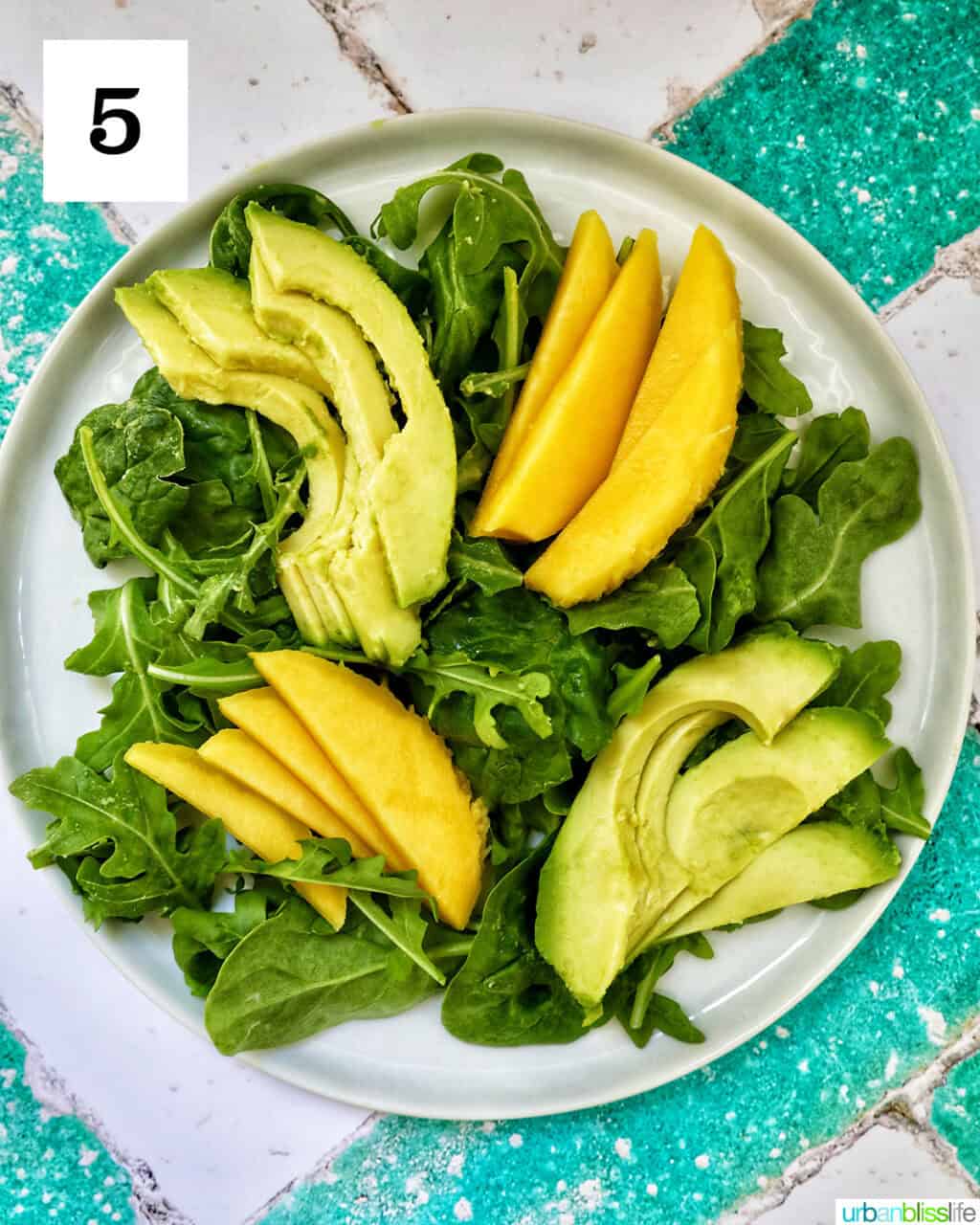 white plate with mixed greens and mango and avocado.
