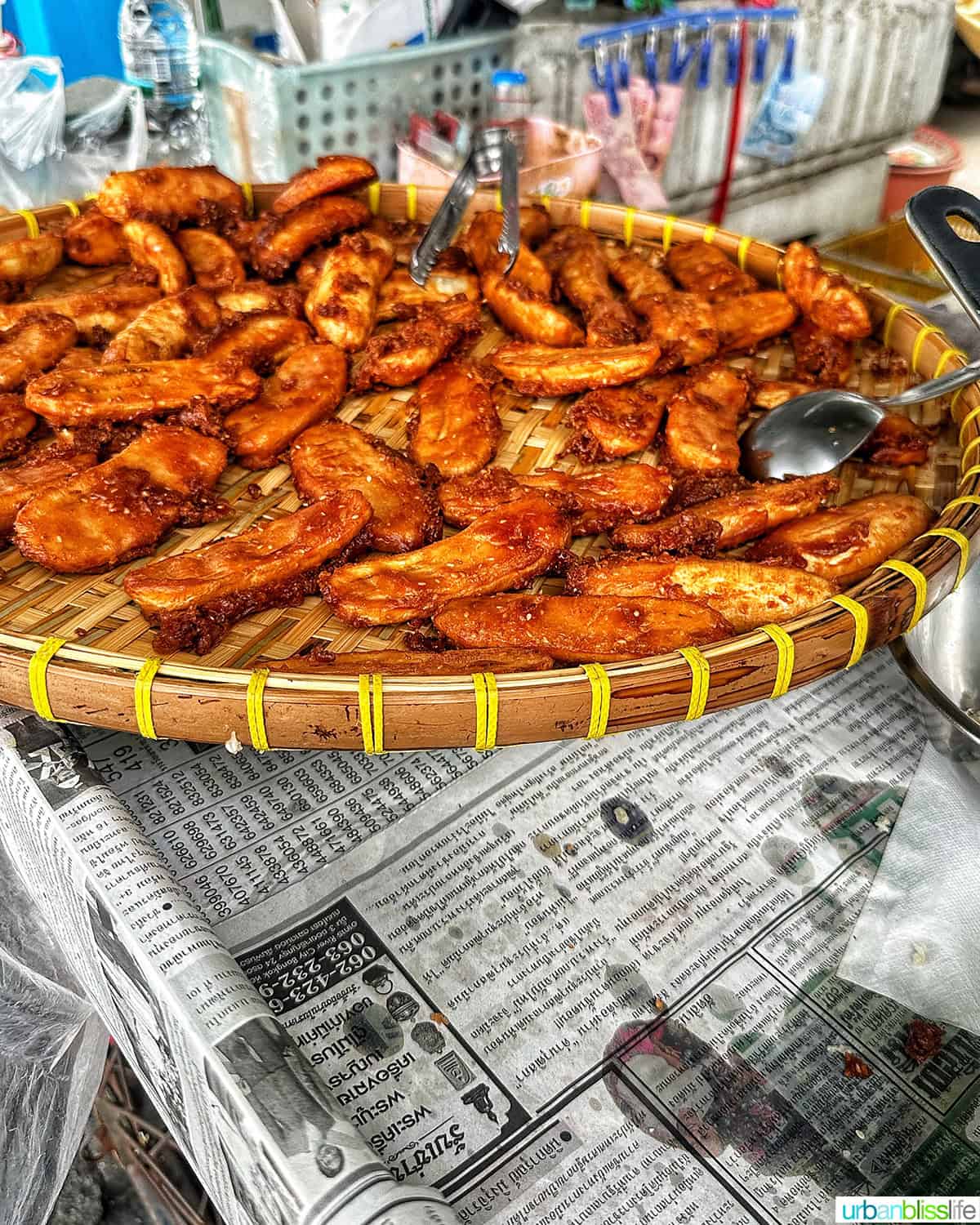 Thai fried bananas in a large platter on top of oil-stained newspapers after being fried.