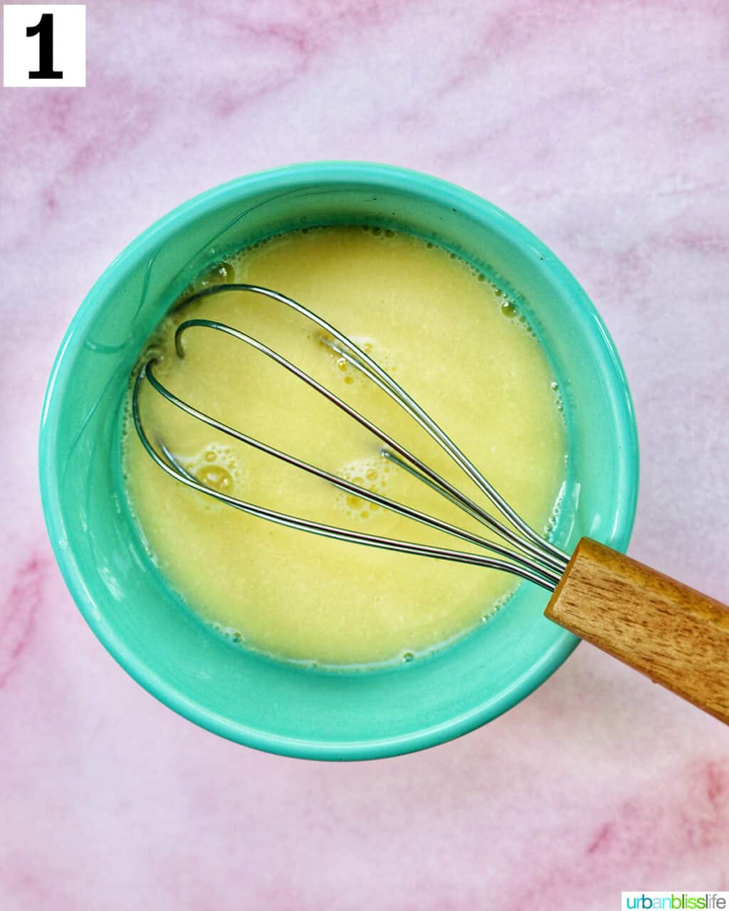 whisk in a bowl of egg wash on pink background.