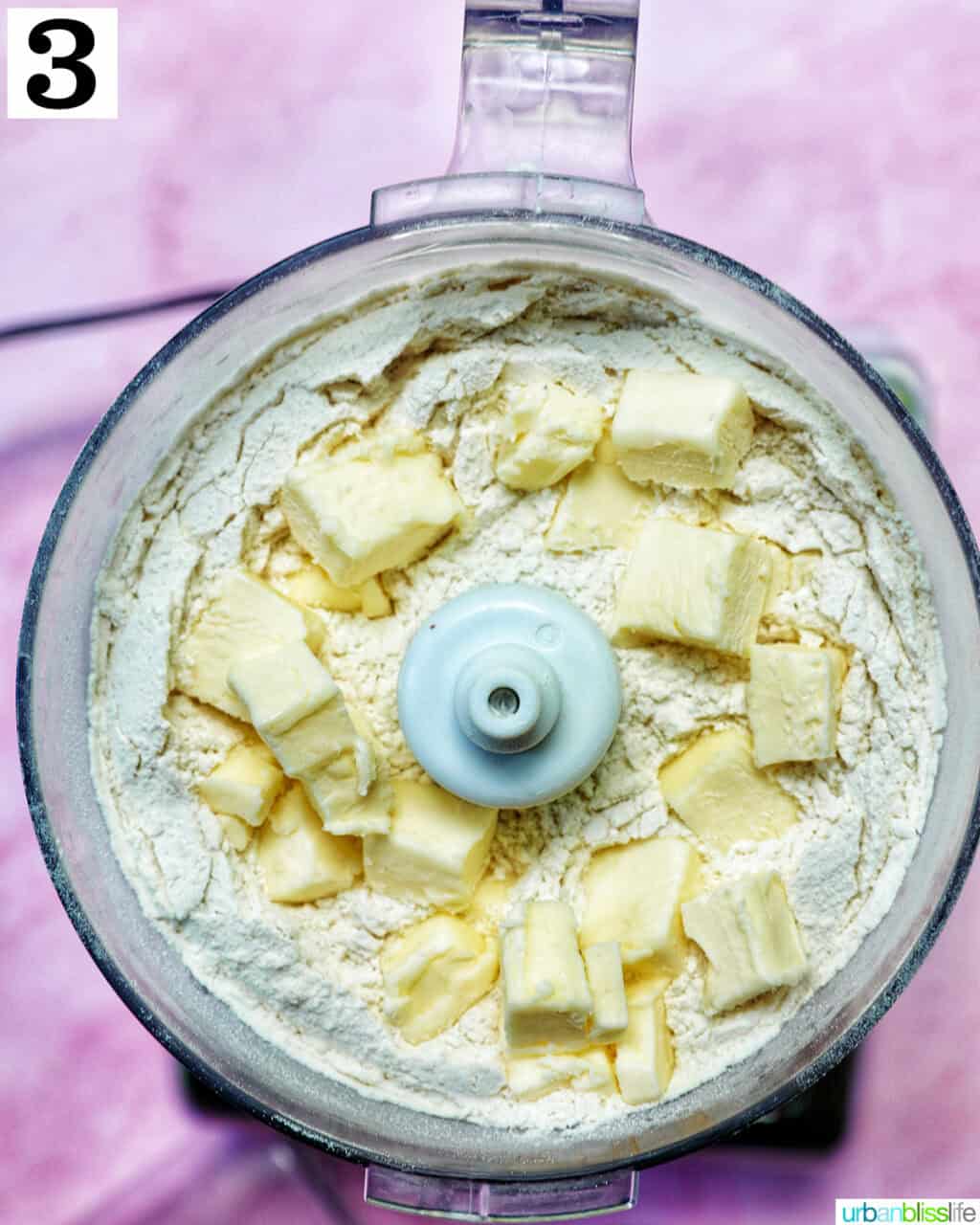 added butter to pie dough in a food processor on a pink background.