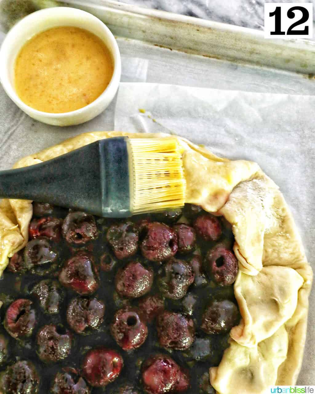 pastry brush brushing egg wash onto the edges of pie dough of a galette.
